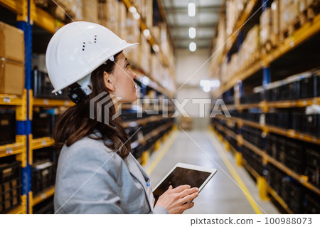 Manager woman in suit controlling goods in a waehouse. 100988073