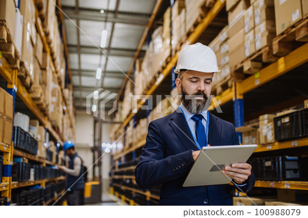 Manager in suit controlling goods in a waehouse. 100988079
