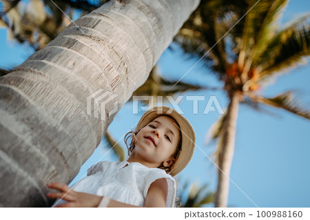 Happy little girl hugging palm tree during tropical vacation. Happy little girl hugging palm tree during tropical vacation. 100988160