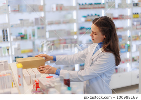 Young pharmacist checking medicine stock in pharmacy. 100988169