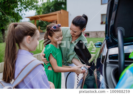 Happy mother showing her little daughters how to charge their electric car. Happy mother showing her little daughters how to charge their electric car. 100988259
