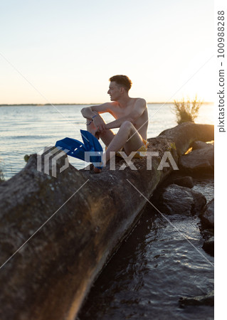 Young man sitting on tree stump in lake. Young man sitting on tree stump in lake. 100988288