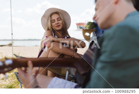 Young couple sitting together in front of van, camping and playing at guitair. Young couple sitting together in front of van, camping and playing at guitair. 100988295