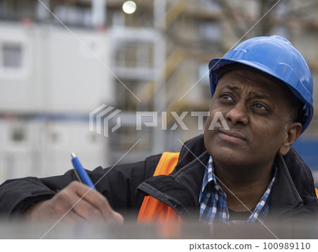 Indian engineer wearing protective workwear writing his projects and signing documents, outdoors Indian engineer wearing protective workwear writing his projects and signing documents, outdoors 100989110