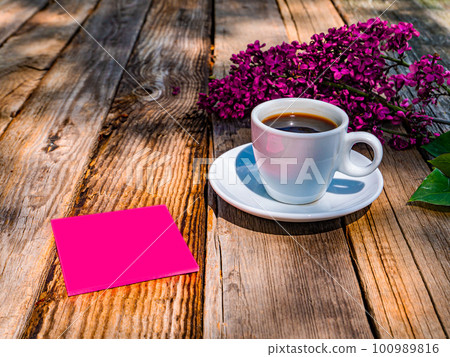 A cup of coffee and a sheet of paper near a branch of lilac on the table. A cup of coffee and a sheet of paper near a branch of lilac on the table. 100989816
