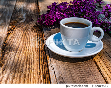 A cup of coffee and a blossoming branch of lilacs on a wooden table. A cup of coffee and a blossoming branch of lilacs on a wooden table. 100989817