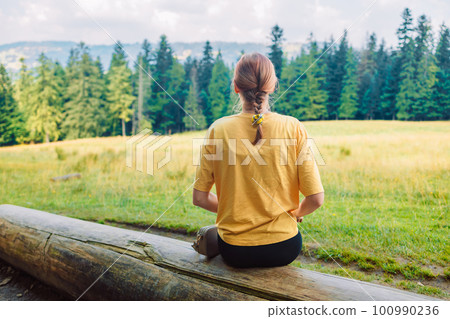 Outdoor leisure activity in mountains holiday vacation. Woman sitting on the wood and admiring landscape. Beautiful nature park in background with top valley and sky. Copy space scenic place 100990236