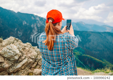 Young woman hiker use smartphone taking photo on seaside mountain top Young woman hiker use smartphone taking photo on seaside mountain top 100990242