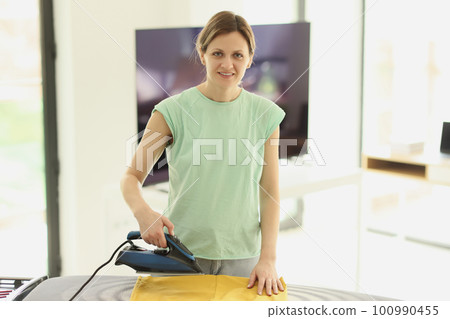 Woman irons washed dried clothes with appliance on board Woman irons washed dried clothes with appliance on board 100990455