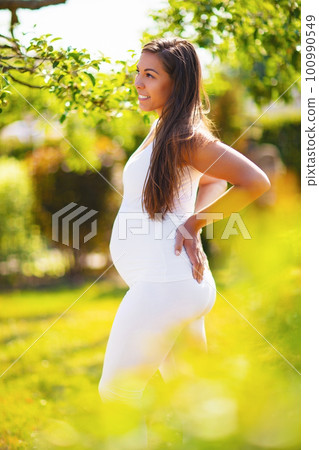 Pregnant woman in beautiful garden looking down at her belly Pregnant woman in beautiful garden looking down at her belly 100990549
