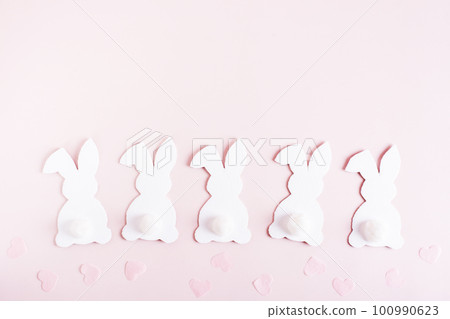 Happy easter white cardboard bunnies in a row and hearts on pink background top view Happy easter white cardboard bunnies in a row and hearts on pink background top view 100990623