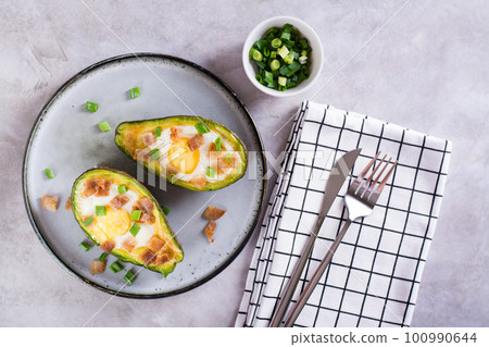 Baked avocado with egg, bacon and chives on a plate on the table for a keto diet top view 100990644