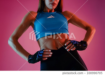 Close up of sporty slim young fitness woman standing, holding hands on waist on studio background Close up of sporty slim young fitness woman standing, holding hands on waist on studio background 100990705