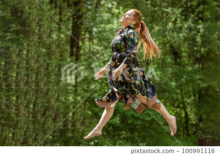 Beautiful happy woman jumps on trampoline outdoor at summer. 100991116