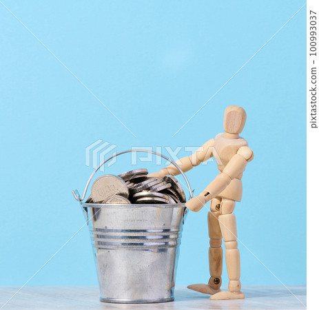 A wooden mannequin and coins in a miniature bucket on a blue background, a concept of high income, subsidy 100993037