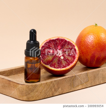 Brown glass bottle with a pipette and half of a red orange on a beige background, oils and cosmetics Brown glass bottle with a pipette and half of a red orange on a beige background, oils and cosmetics 100993054