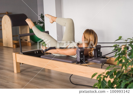 Woman training pilates on the reformer bed. Reformer pilates studio machine for fitness workouts in gym. Fit, healthy and strong authentical body. Fitness concept Woman training pilates on the reformer bed. Reformer pilates studio machine for fitness workouts in gym. Fit, healthy and strong authentical body. Fitness concept 100993142