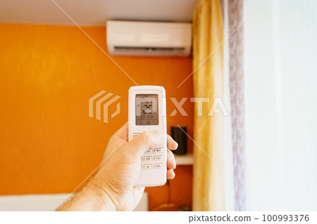 hand with the remote control of the air conditioner.  100993376