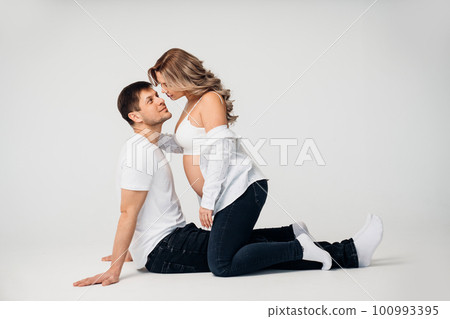 a blonde pregnant woman with a man sitting on the floor in a white room. a blonde pregnant woman with a man sitting on the floor in a white room. 100993395
