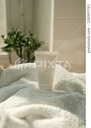 White cream tube and towel in real room interior mock-up, beauty and care product packaging template 100993761