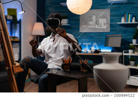 Professional artist of plastic arts looking for new drawing techniques in metaverse with virtual reality visors. African american sketch student using online universe to create artwork. Professional artist of plastic arts looking for new drawing techniques in metaverse with virtual reality visors. African american sketch student using online universe to create artwork. 100994522