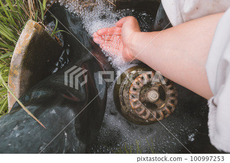 A farmer washing his feet at the water inlet of the rice field 100997253