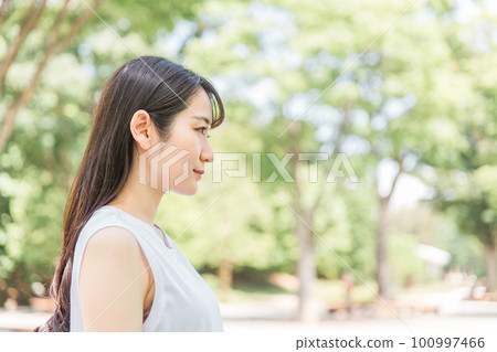 A black-haired woman with a serious expression standing in the fresh greenery 100997466