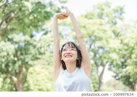 A woman who stretches, warms up, and takes a deep breath in the fresh green A woman who stretches, warms up, and takes a deep breath in the fresh green 100997634