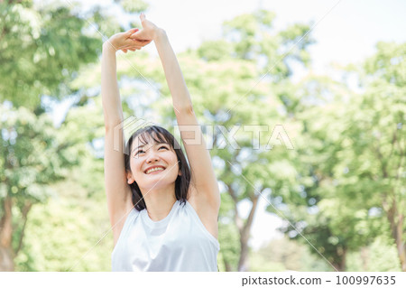 A woman who stretches, warms up, and takes a deep breath in the fresh green 100997635