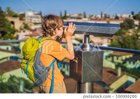 Boy tourist looks through binoculars in Old town Kaleici in Antalya. Turkiye. Panoramic view of Antalya Old Town port, Taurus mountains and Mediterrranean Sea, Turkey. Traveling with kids concept Boy tourist looks through binoculars in Old town Kaleici in Antalya. Turkiye. Panoramic view of Antalya Old Town port, Taurus mountains and Mediterrranean Sea, Turkey. Traveling with kids concept 100998200