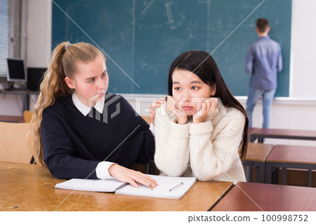 Tired female students during writing notes in classroom 100998752