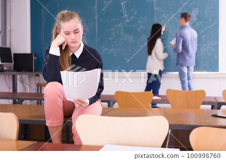Frustrated girl student sitting in classroom with paper 100998760