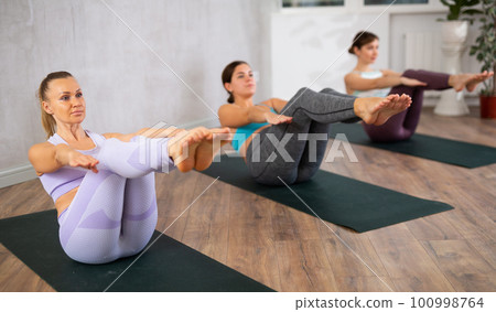 Diligent women practicing upward boat pose of yoga in light fitness room Diligent women practicing upward boat pose of yoga in light fitness room 100998764