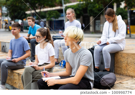Students record lecture while sitting on a stone street parapet Students record lecture while sitting on a stone street parapet 100998774