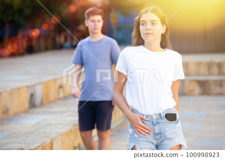 Cute teen girl in denim shorts walking down street 100998923