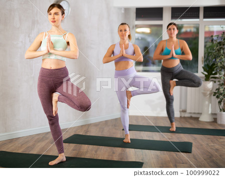 Girl exercising with group at yoga studio, standing in warrior one leg pose on fitness mat 100999022