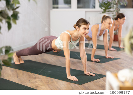Diligent women practicing plank pose of yoga in light fitness room 100999177