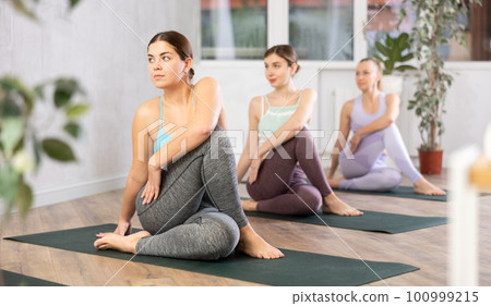 Diligent women practicing lord of the fishes pose of yoga in light fitness room 100999215