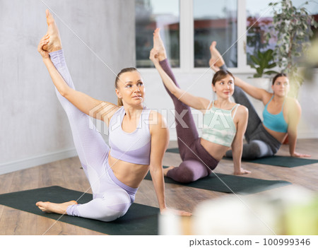 Young woman practicing stretching yoga postures at group class 100999346