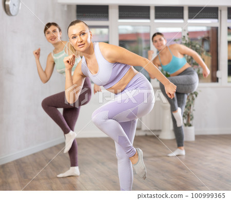 Smiling woman practicing rhythmic aerobics during group workout Smiling woman practicing rhythmic aerobics during group workout 100999365