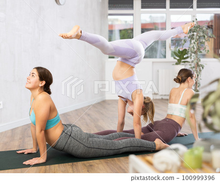 Young women doing handstand split and Adho Mukha Shvanasana 100999396