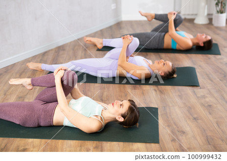 Woman doing Ardha Pawanmuktasana with group in yoga studio 100999432