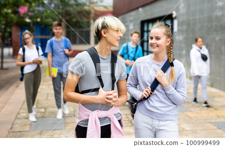 Teen schoolmates with backpacks and workbooks walking to college 100999499