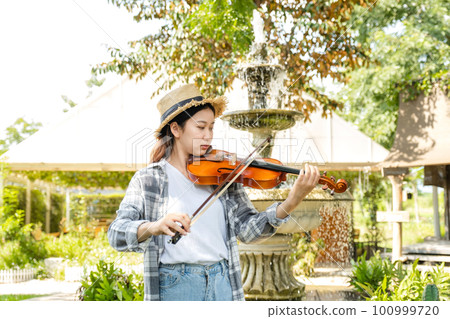 Close-up portrait of Young Asia woman music violinist play violin, relax in the garden with peace of mind 100999720
