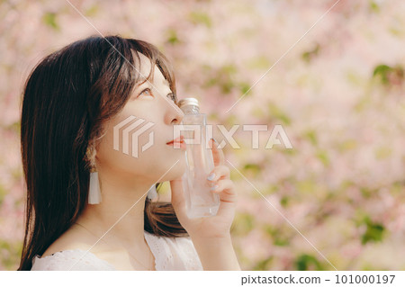 Woman holding a makeup bottle under the cherry blossom tree Woman holding a makeup bottle under the cherry blossom tree 101000197