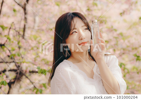 Woman holding a makeup bottle under the cherry blossom tree 101000204