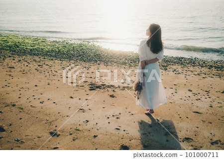 A woman holding dried flowers and staring at the sea 101000711