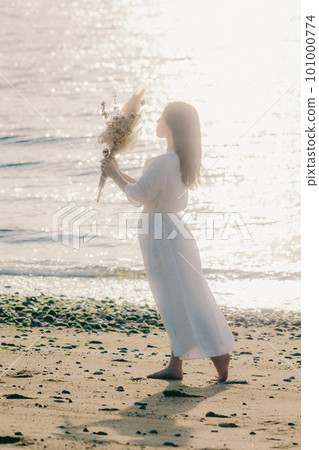 A woman holding dried flowers and staring at the sea A woman holding dried flowers and staring at the sea 101000774