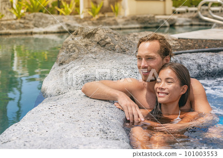 Spa couple luxury wellness retreat resort relaxing in hot tub at luxury hotel. Happy Asian woman and Caucasian man at pool vacation 101003553