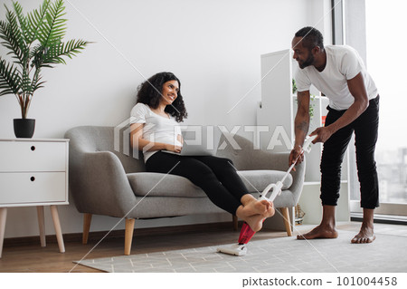 Smiling woman working on laptop while man vacuuming carpet Smiling woman working on laptop while man vacuuming carpet 101004458